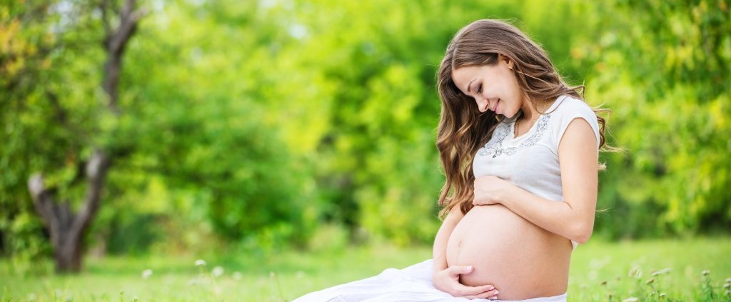 Pregnant woman sitting on a lawn addressing pregnancy concerns, lovingly looking at her belly, surrounded by nature