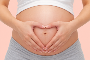 Pregnant woman forming a heart shape with her hands over her baby bump