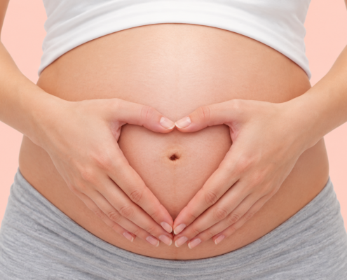 Pregnant woman forming a heart shape with her hands over her baby bump
