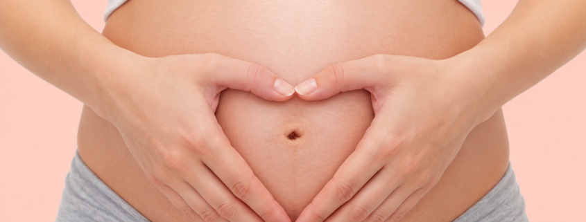 Pregnant woman forming a heart shape with her hands over her baby bump