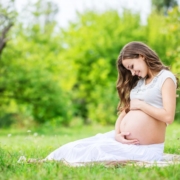 Pregnant woman sitting on a lawn addressing pregnancy concerns, lovingly looking at her belly, surrounded by nature